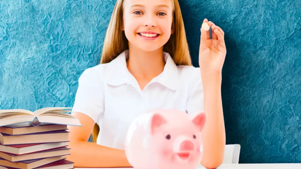 uma mão segurando um menina cofrinho em forma de porquinho e com livros ao lado.