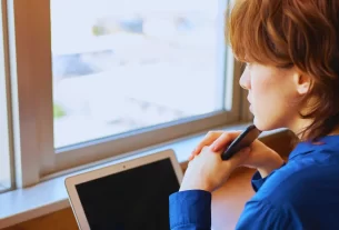 Detox Digital: Mulher desconectando do celular e olhando pela janela em um momento de paz, representando o detox digital