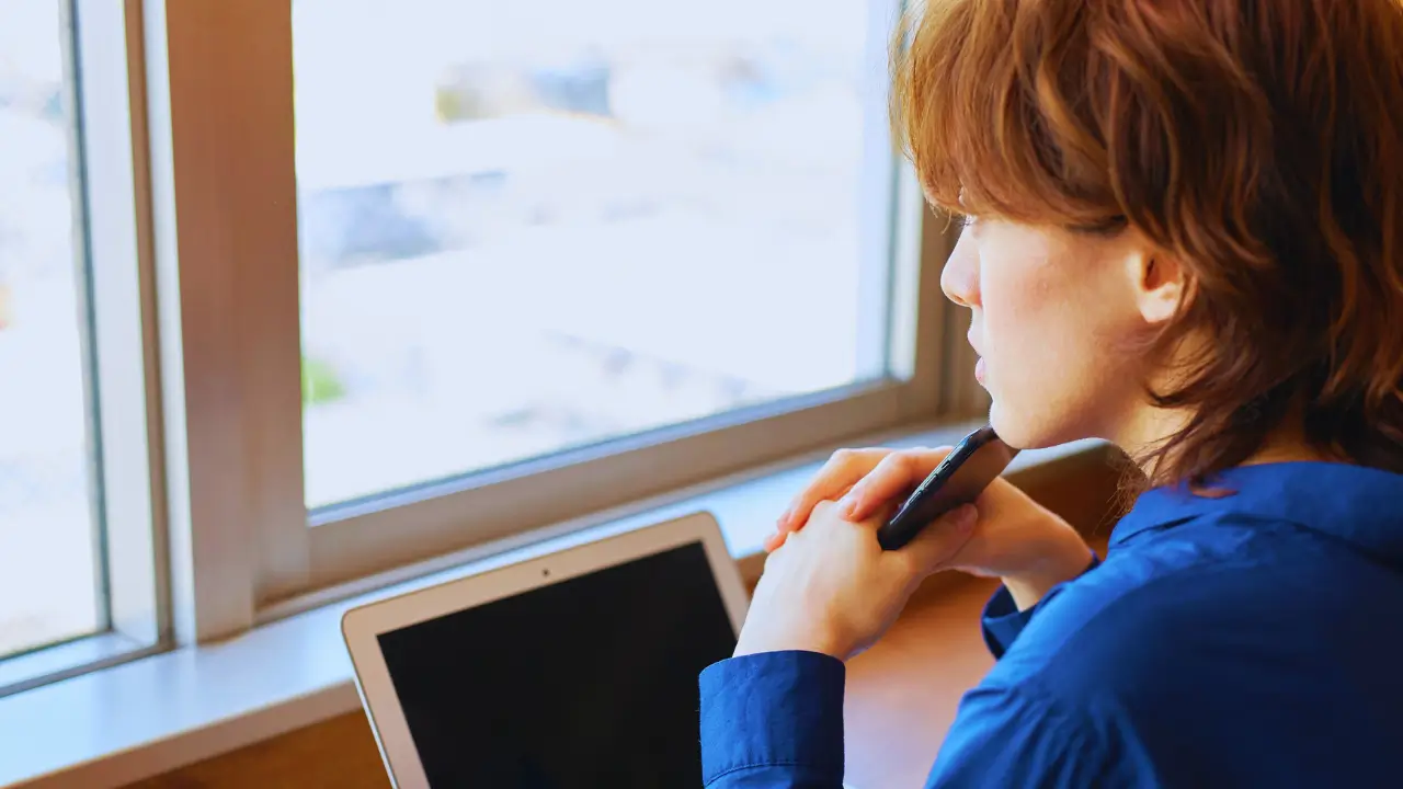Detox Digital: Mulher desconectando do celular e olhando pela janela em um momento de paz, representando o detox digital