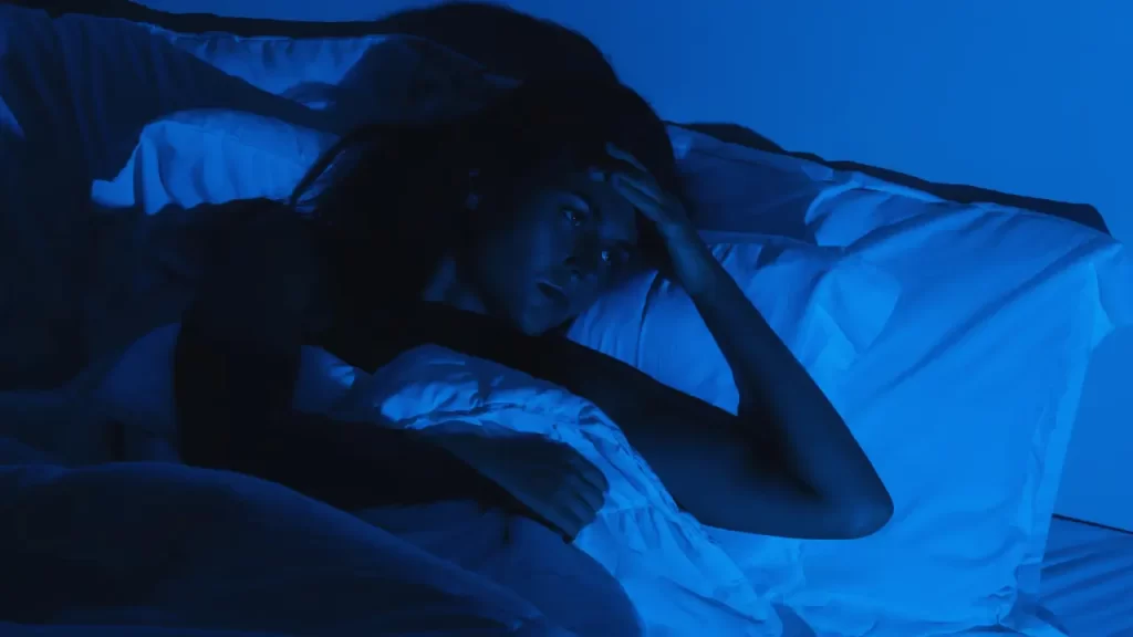 Mulher sozinha deitada na cama, em ambiente escuro e silencioso.