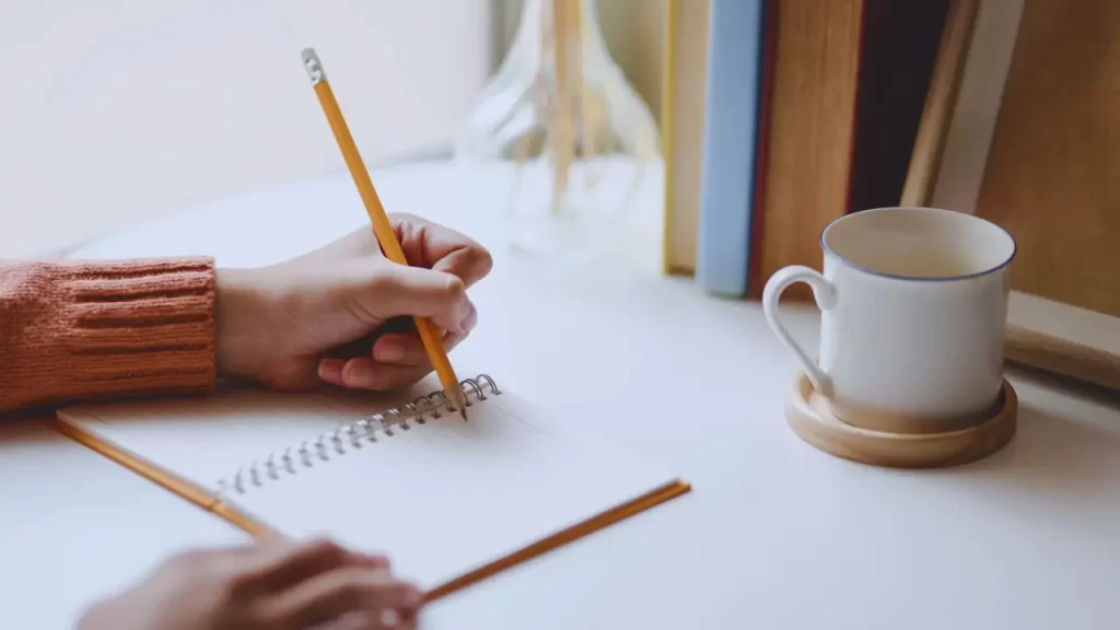 Rotina saudável sem tecnologia. Mãos escrevendo em diário ou agenda de papel, com xícara de chá ao lado