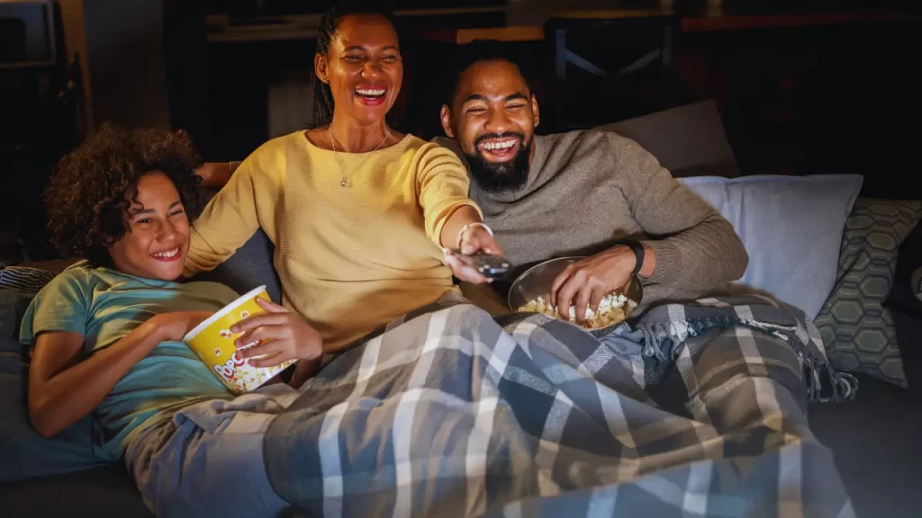 Família assistindo filme em casa com pipoca e cobertores