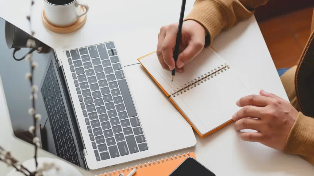 Profissional planejando a mudança de emprego com caderno e computador sobre a mesa